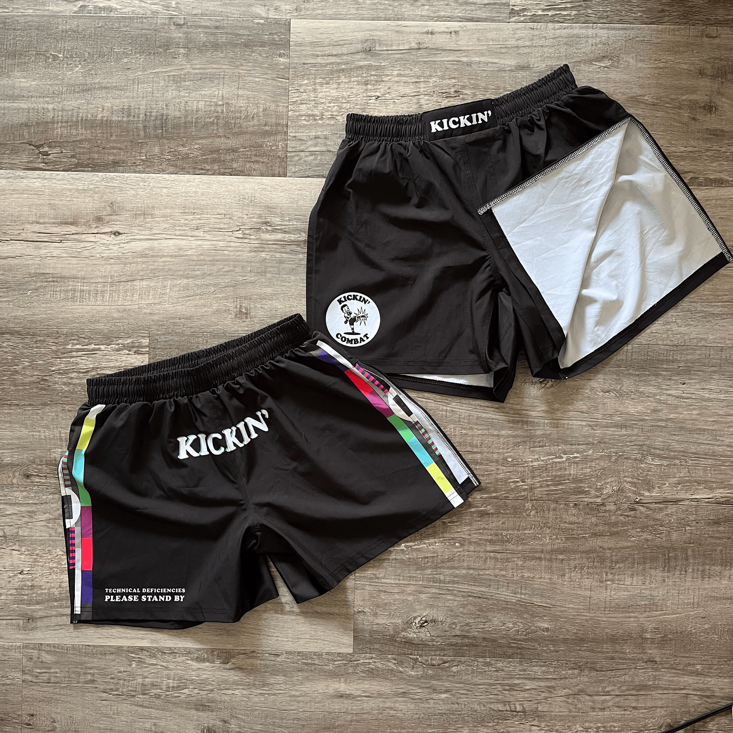 Two pairs of Kickin' Combat high cut gladiator MMA shorts on wood floor